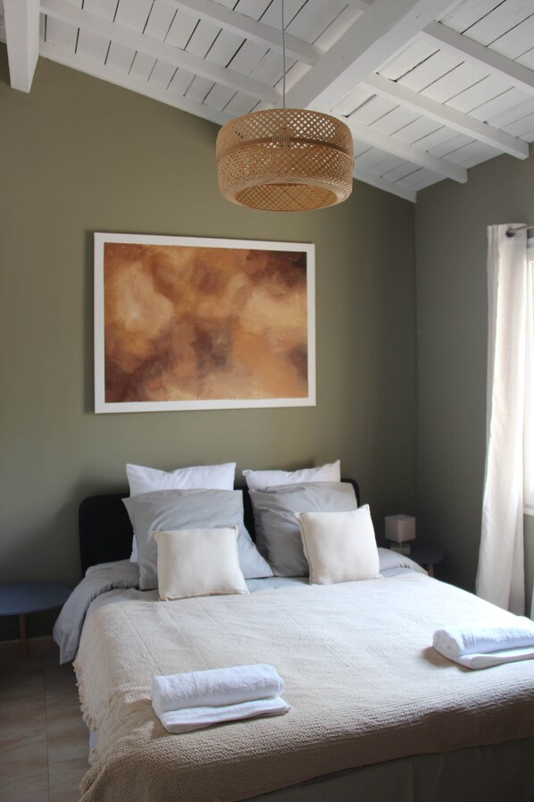 A bedroom with a bed, pillows, a blanket, a wall-mounted artwork, and a ceiling light fixture.
