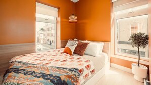 Een slaapkamer met een groot bed, uitzicht op een straat en een potplante.