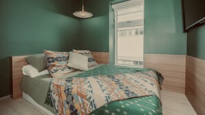 Un dormitorio con cama, almohadas, una lámpara colgante y una ventana con persianas.