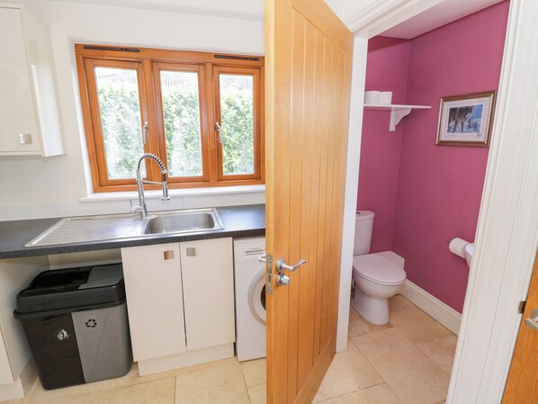A compact kitchen with a sink, a washing machine, and a toilet in a small bathroom. - Filly Brook (Worcester)
