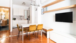 A modern kitchen with white cabinets, a dining area with a white table and yellow chairs, and a mounted flat-screen TV. - Levante 65 by Wonderful Italy (Bari)