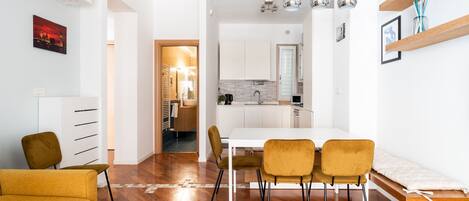 Una sala de estar moderna con un sofá, una mesa de comedor con sillas y una cocina al fondo.