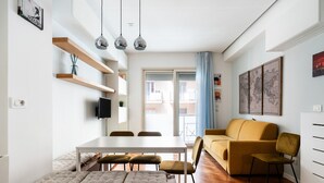 A modern living room with a dining table, sofa, and chairs. There are shelves with decorative items and a flat-screen TV mounted on the wall. - Levante 65 by Wonderful Italy (Bari)