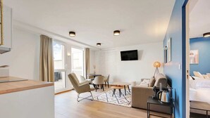 A modern hotel room with a wooden floor, a sofa, a dining table, and a TV mounted on the wall. - Suite Raphaël #4- Rooftop & Air Conditioning (Vanves)