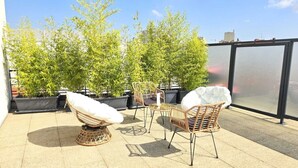 A rooftop terrace with wicker furniture, potted plants, and a glass enclosure. - Suite Raphaël #4- Rooftop & Air Conditioning (Vanves)