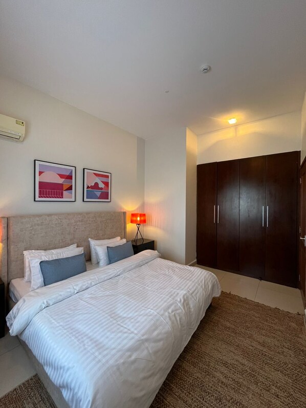 A hotel room with a large bed, two pillows, a nightstand with a lamp, a wardrobe, and two framed pictures on the wall.