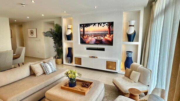 Ein modernes Wohnzimmer mit großem Flachbildfernseher, beigen Sofas, einem Couchtisch und dekorativen Vasen.