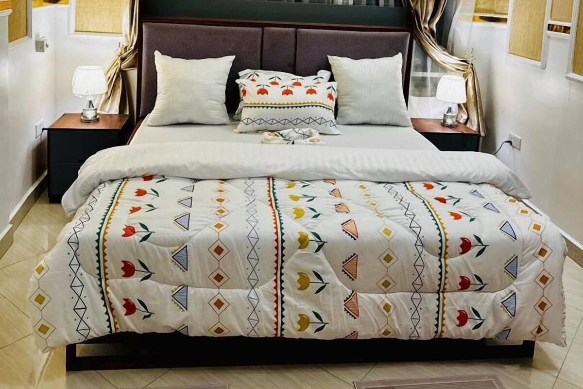 Habitación de hotel con una cama grande, un cabecero, dos mesitas de noche con lámparas y una ventana con cortinas.