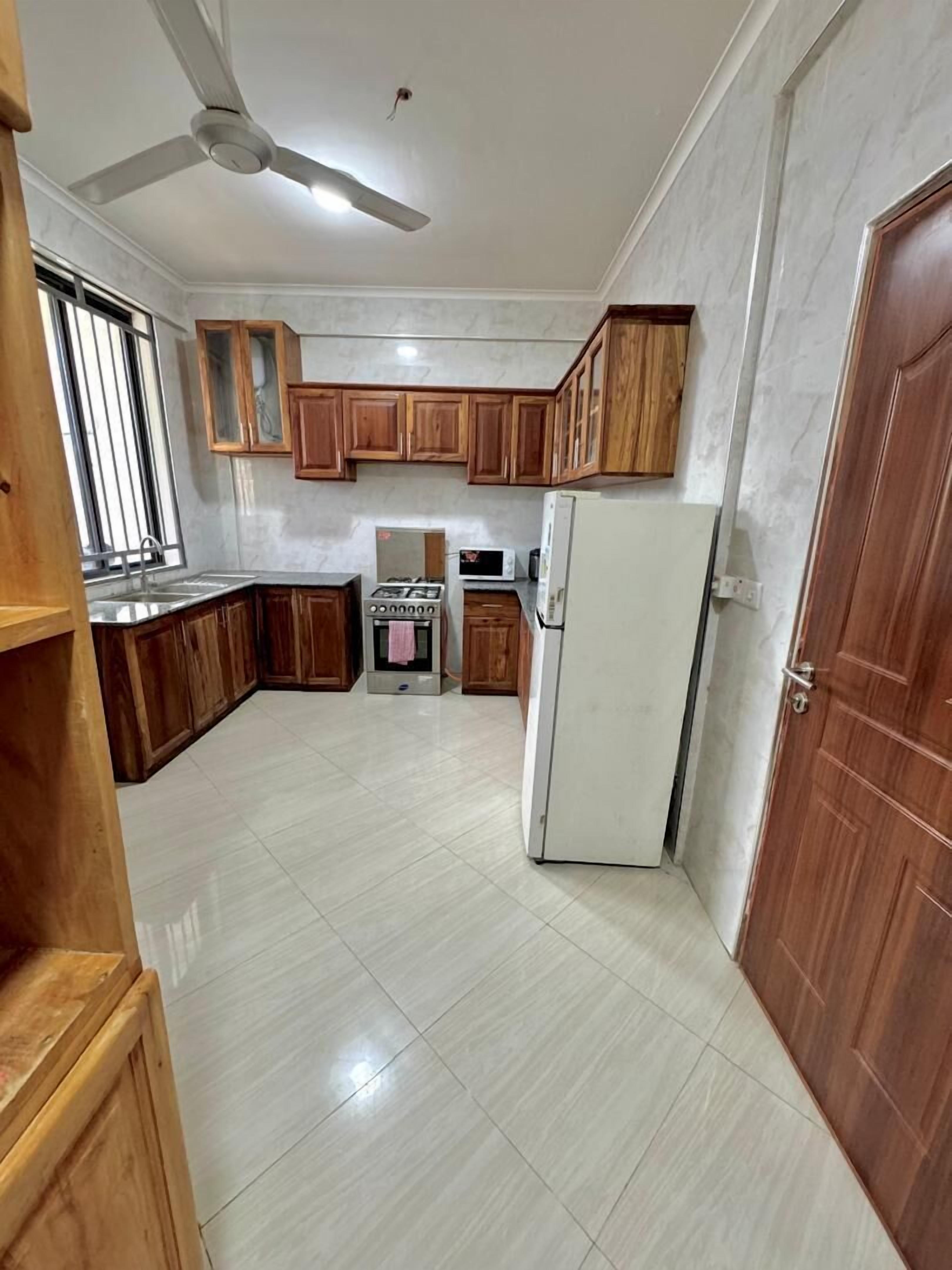 A kitchen with wooden cabinets, a gas stove, a microwave, and a refrigerator.