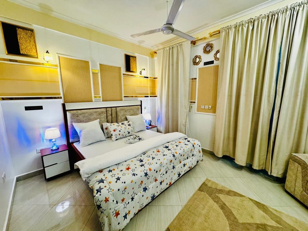 A hotel room with a bed, bedside tables, a ceiling fan, and curtains.