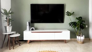 A modern living room with a flat-screen TV mounted on the wall, a white console table, two small round tables, and potted plants. - Residence City Luna, Apartment (Rodos)