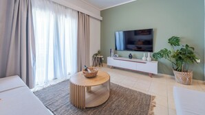 A modern living room with a round wooden coffee table, a flat-screen TV mounted on the wall, a white sofa, and a potted plant. - Residence City Luna, Apartment (Rodos)
