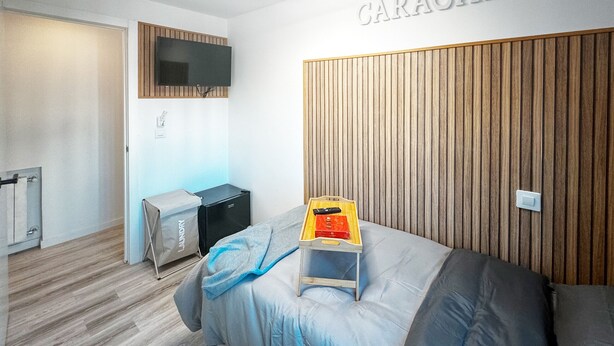 A hotel room with a bed, a TV mounted on the wall, a wooden headboard, and a small table with a remote control. - Caracas: perfect room to live and share in Madrid (Madrid)