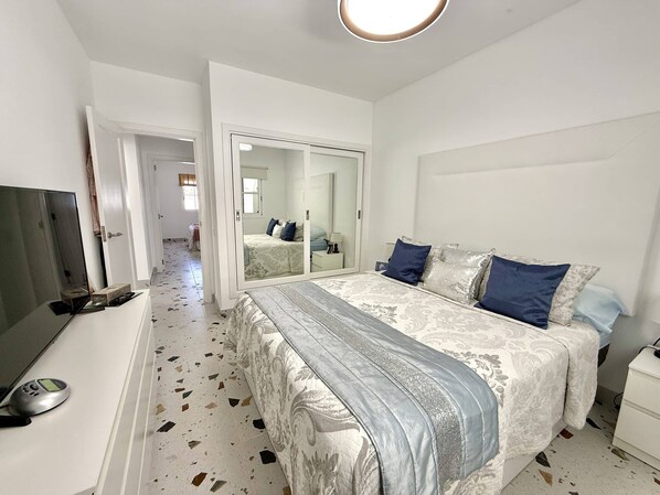 A bedroom with a bed, a TV, a wardrobe, and a mirror.