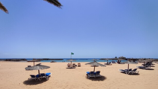 A beach with sun loungers and umbrellas, a flag, and a clear sky. - Villa Stay&Enjoy (Caleta de Fuste)