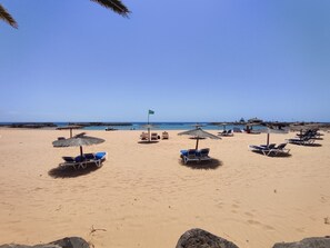 A beach with sun loungers and umbrellas, a flag, and a clear sky.