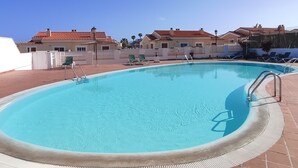 A swimming pool with a tiled deck, surrounded by lounge chairs and a fence. - Villa Stay&Enjoy (Caleta de Fuste)