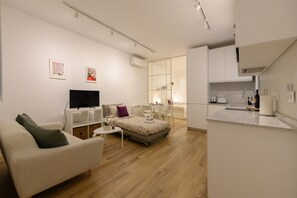 A modern, well-lit living room with a sofa, a small table, and a TV. There is a kitchen area with a counter and cabinets. - 1 bedroom flat in the centre of Madrid (Madrid)