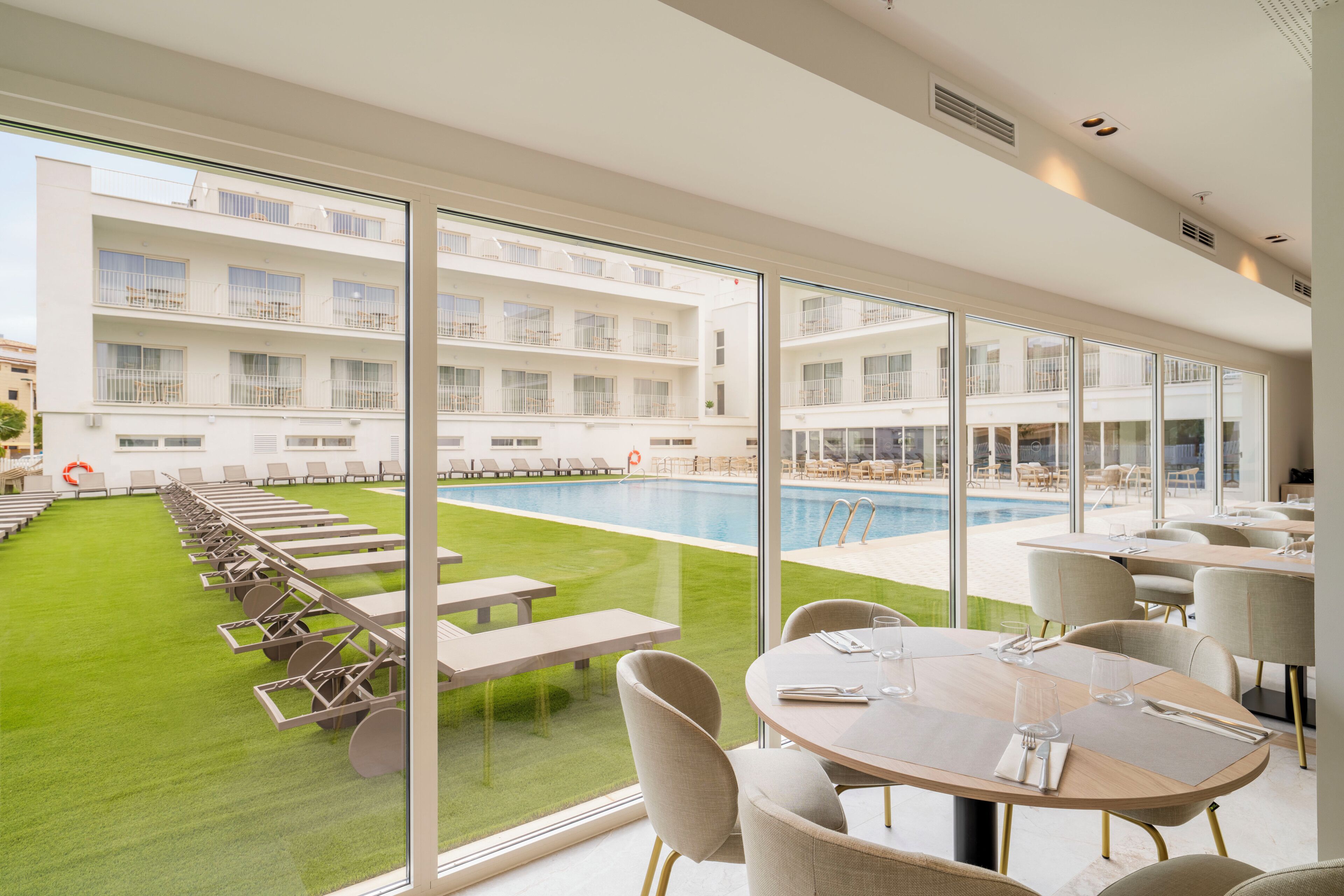 A hotel room with a large window overlooking a swimming pool and a well-maintained lawn.