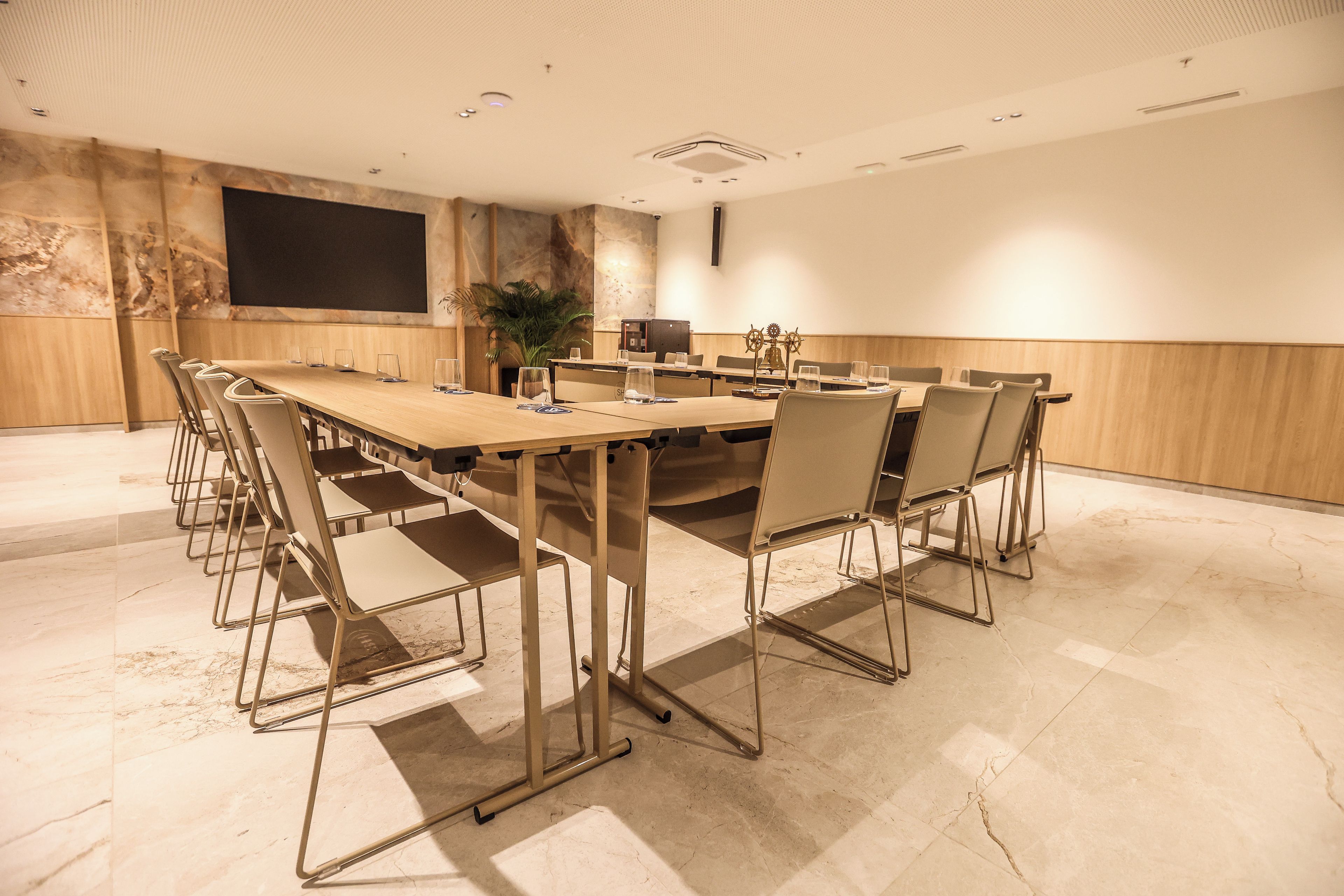 A conference room with a long table, chairs, a projector screen, and a plant.