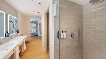 Un baño moderno con cabina de ducha de vidrio, tocador con espejo y un banco.