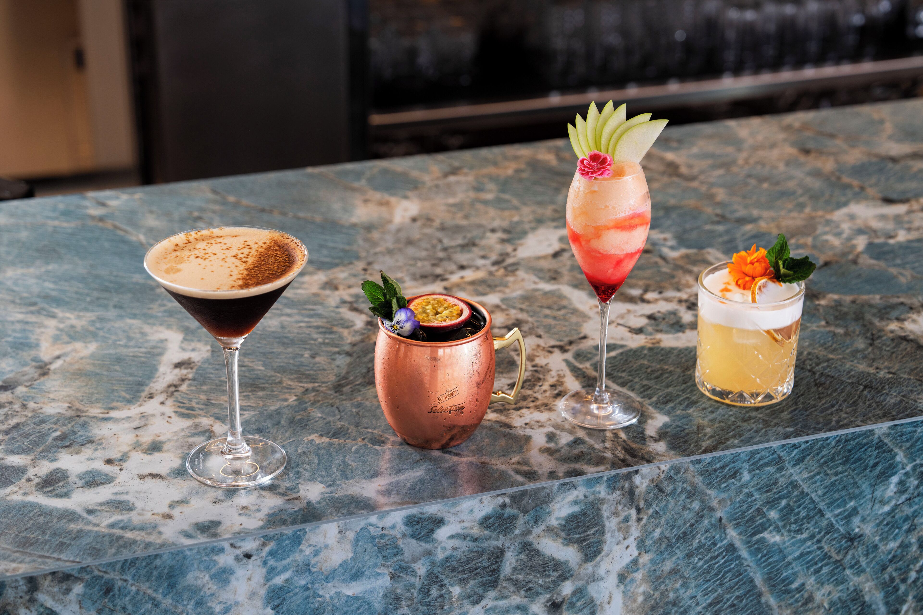 A bar area with a marble countertop, three drinks, and a copper mug.
