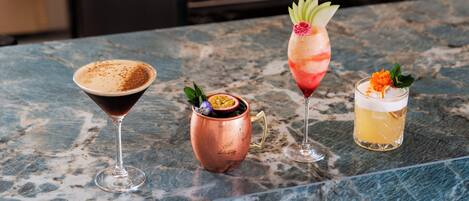 A bar area with a marble countertop, three drinks, and a copper mug.