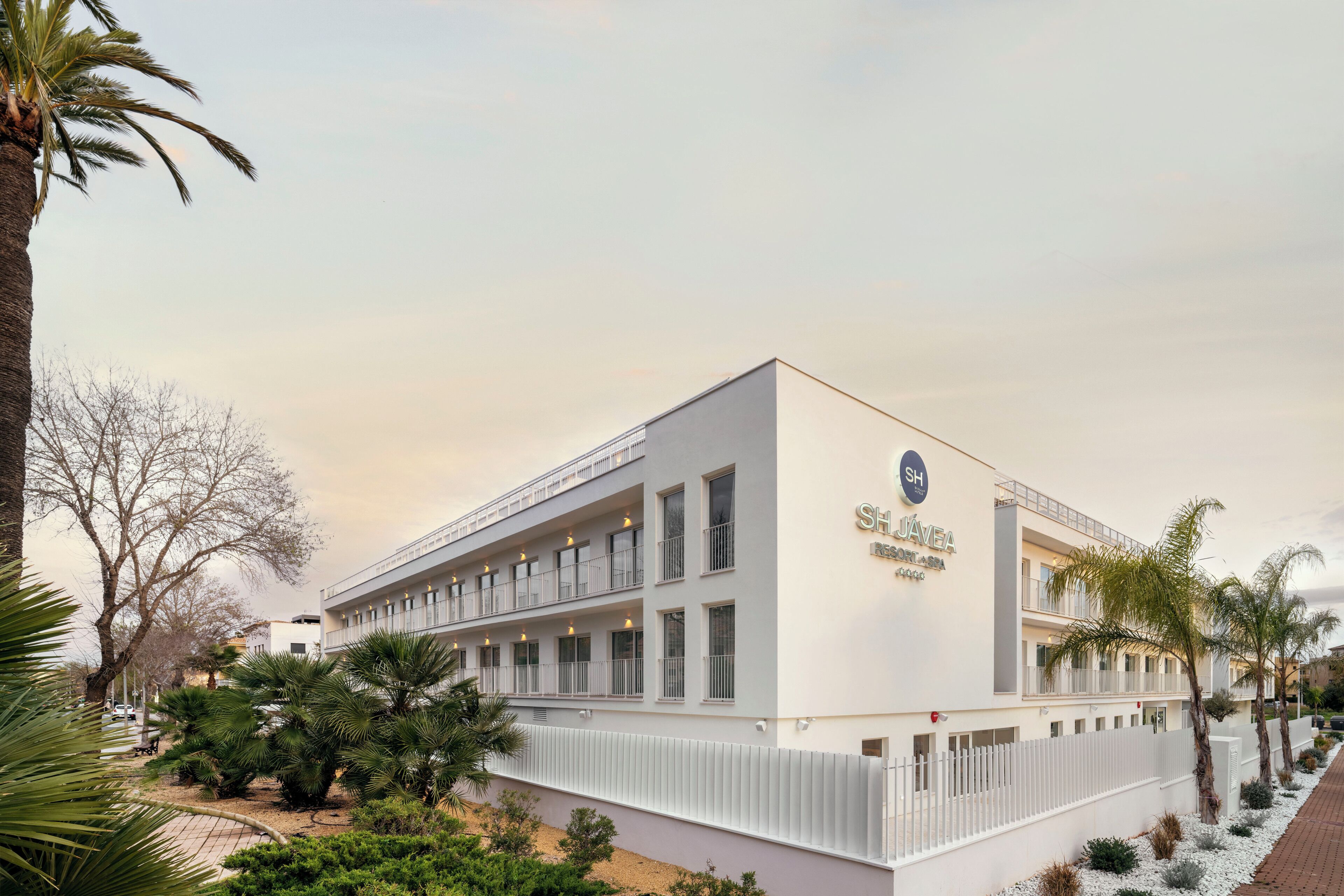 Een modern hotel met een witte gevel, meerdere balkons en een bord dat aangeeft dat het een hotel is.
