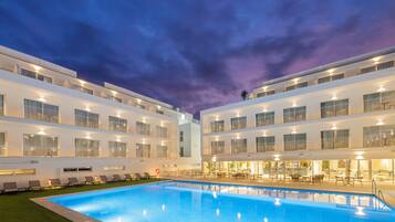 A modern hotel with a swimming pool, multiple balconies, and outdoor seating areas.