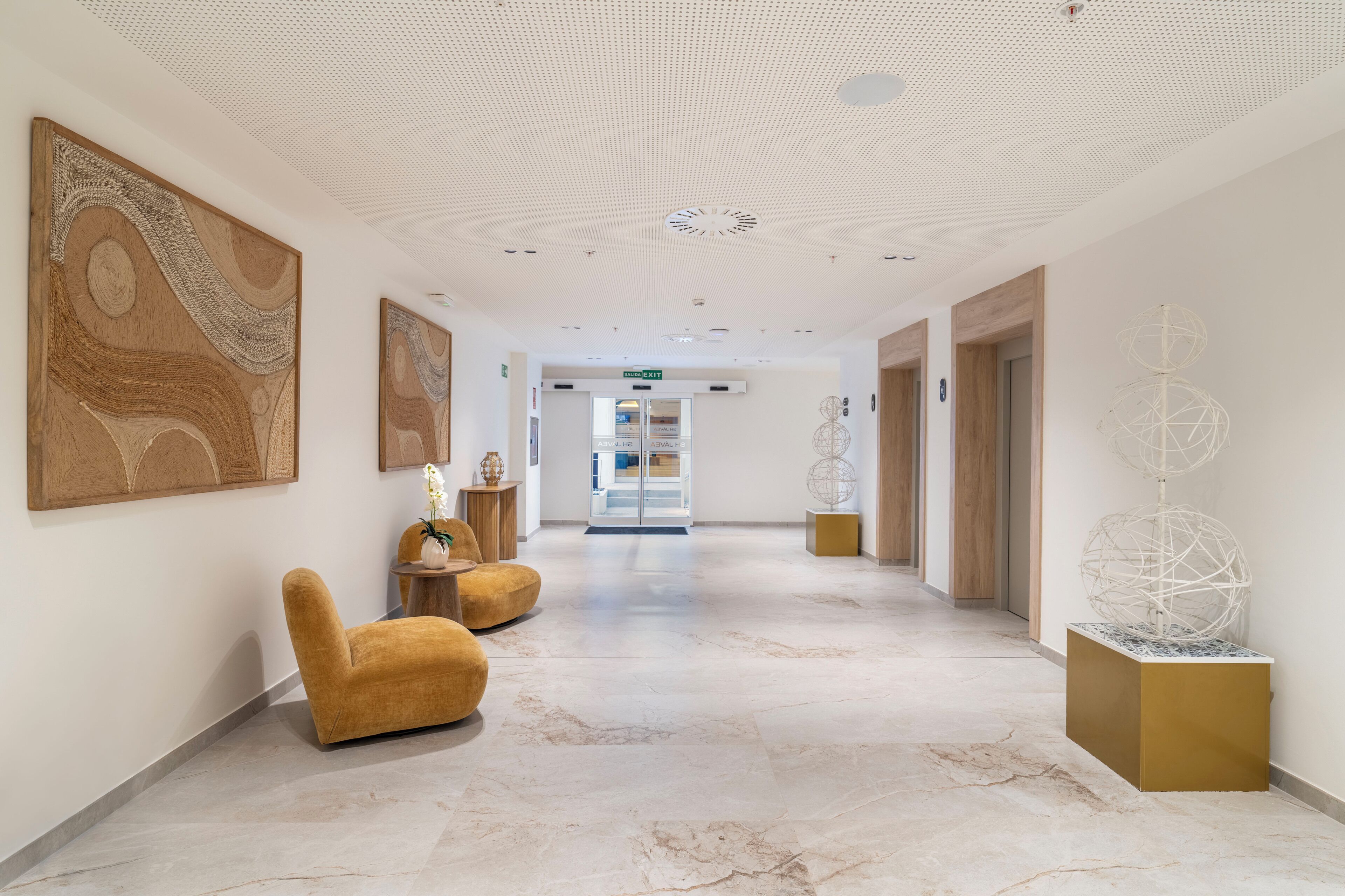 A modern hotel lobby with marble flooring, a central seating area, and contemporary artwork.