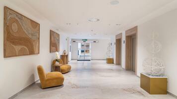 A modern hotel lobby with marble flooring, a central seating area, and contemporary artwork.