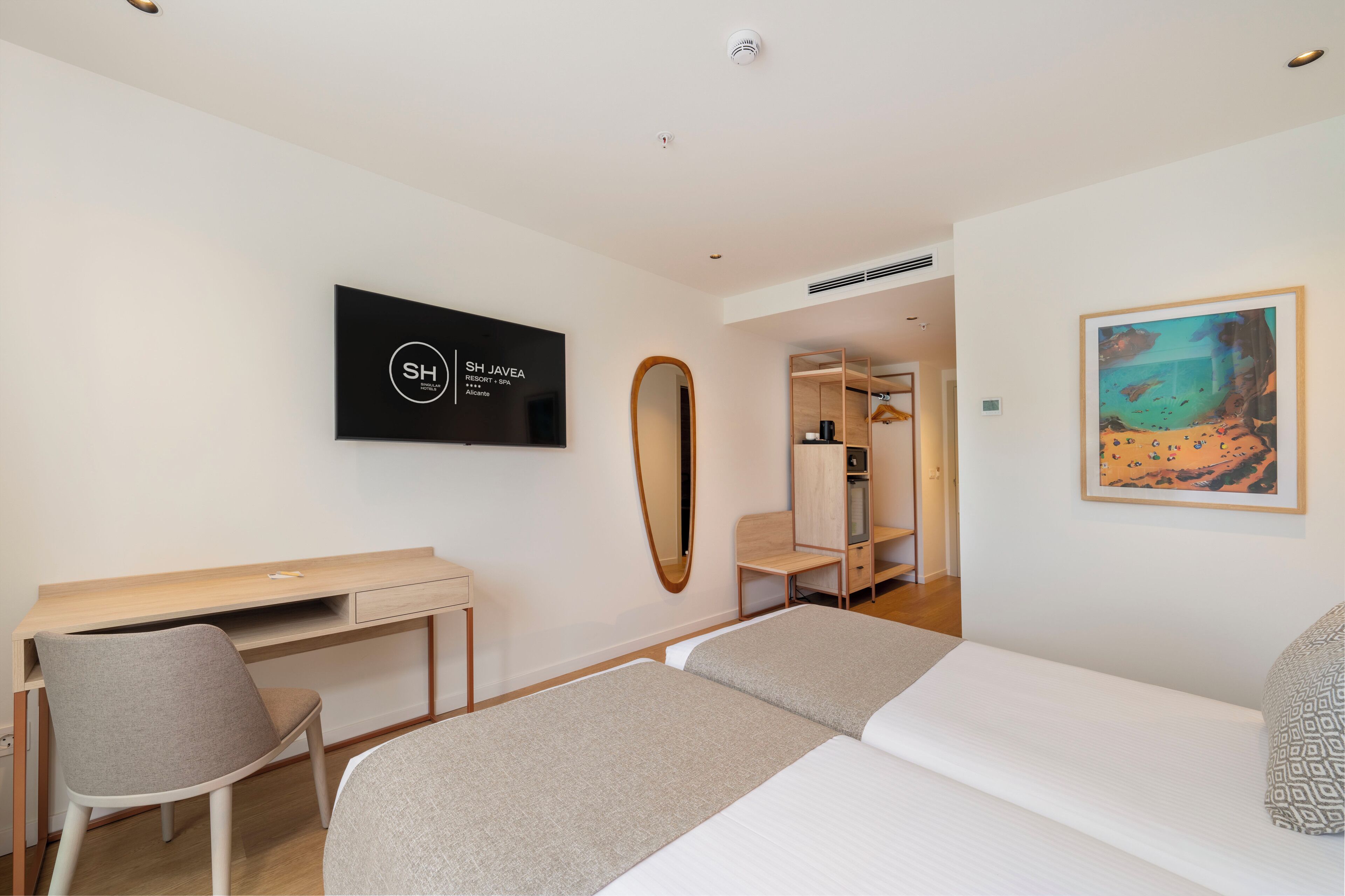 Una habitación de hotel con una cama, un escritorio, una silla, un televisor, un espejo y un cuadro.