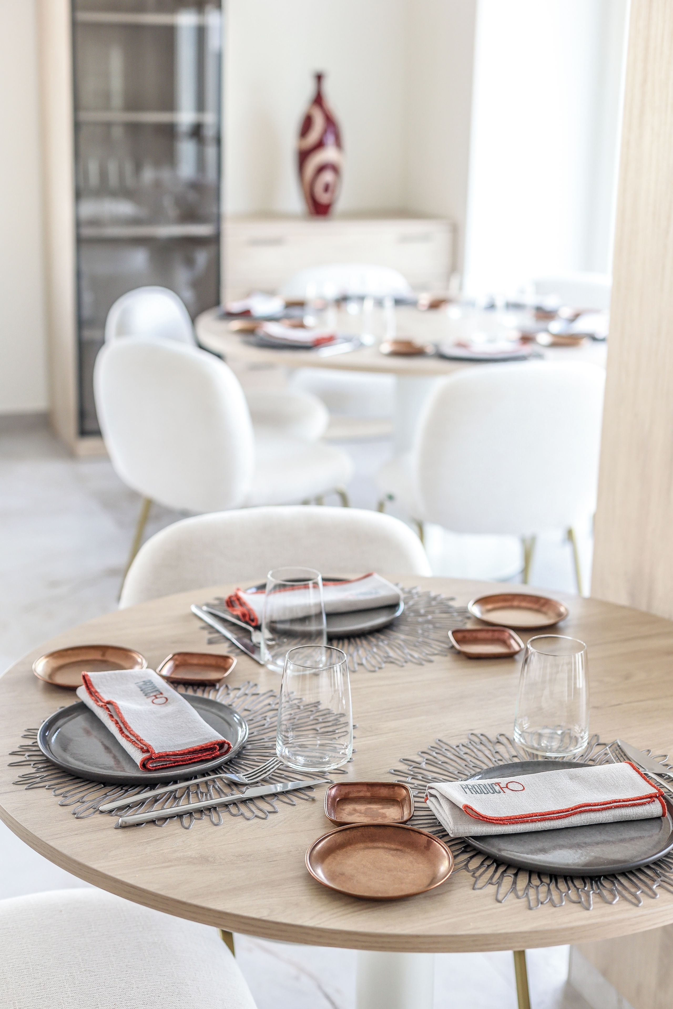 A dining table set with plates, cutlery, and glasses, surrounded by white chairs in a modern interior.
