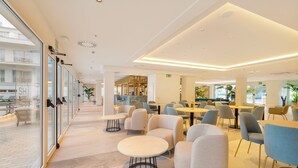 A modern hotel lobby with glass walls, a seating area with round tables, and a bar area. - SH Jávea (Jávea)