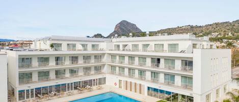 Un hotel con piscina, varios balcones y vistas a la montaña.