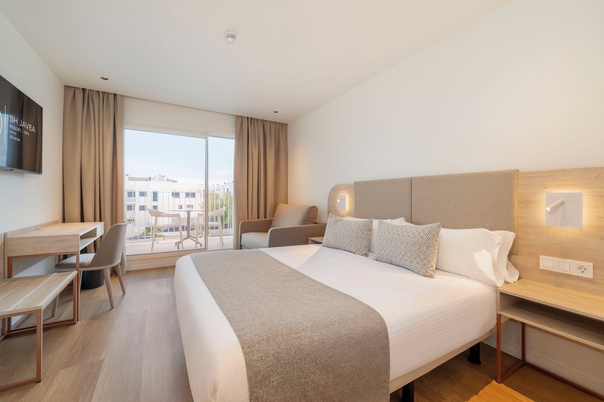 Ein Hotelzimmer mit Bett, Schreibtisch, Stuhl und Fernseher an der Wand.