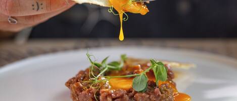 A person holding a piece of food over a plate with a sauce and garnish.