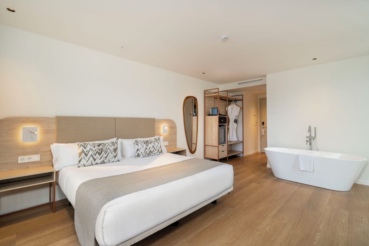 Ein modernes Hotelzimmer mit einem großen Bett, einem eingebauten Kleiderschrank, einem Schminktisch mit Spiegel und einer freistehenden Badewanne.