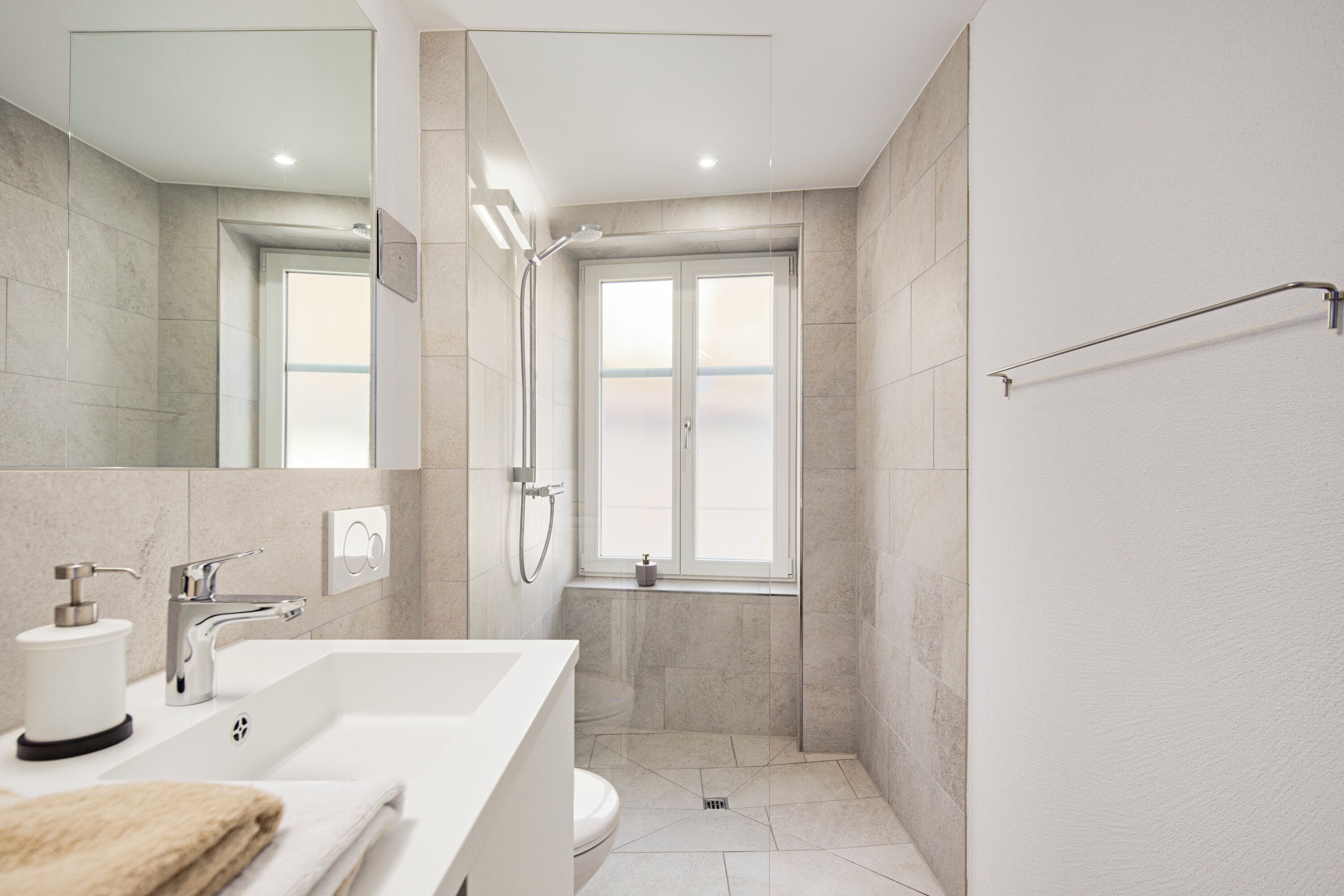 A modern bathroom with a large mirror, a sink, a toilet, and a shower area.