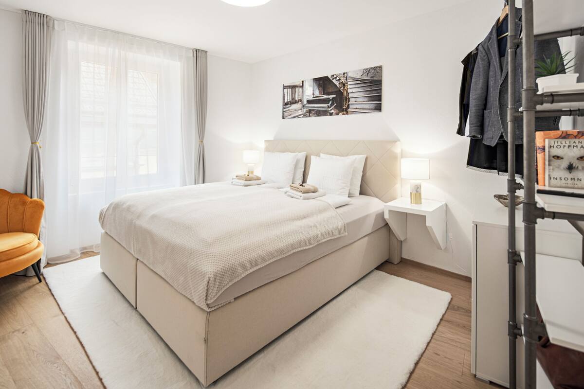 A modern bedroom with a large bed, bedside tables, a chair, and a bookshelf.