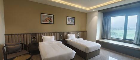 Ein Hotelzimmer mit zwei Betten, einem Sessel, einem kleinen Tisch, einem Deckenventilator und einem Fenster mit Aussicht.