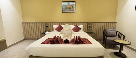 A hotel room with a large bed, a headboard, a bedside table, a chair, a small round table, and a wall-mounted picture.