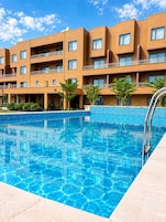 Una piscina con superficie azul cristalina, rodeada por un edificio con varios balcones y fachada de azulejos.