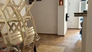 A hallway with a chair and a table, a painting on the wall, and a kitchen area in the background. - APARTMENT IN A QUIET RESIDENCE (Aïn El Turk)
