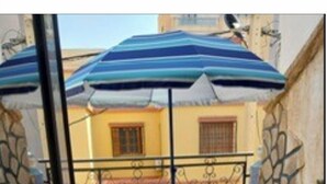 A balcony with a table and chairs, a striped umbrella, and a stone wall. - APARTMENT IN A QUIET RESIDENCE (Aïn El Turk)
