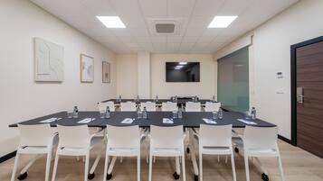 A conference room with a long table, white chairs, and a flat-screen TV on the wall.