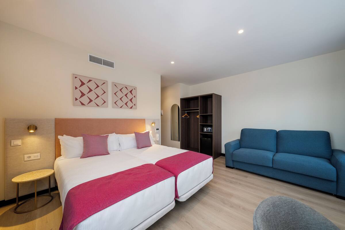 Une chambre d’hôtel avec un grand lit, un canapé bleu, une petite table ronde et une armoire.