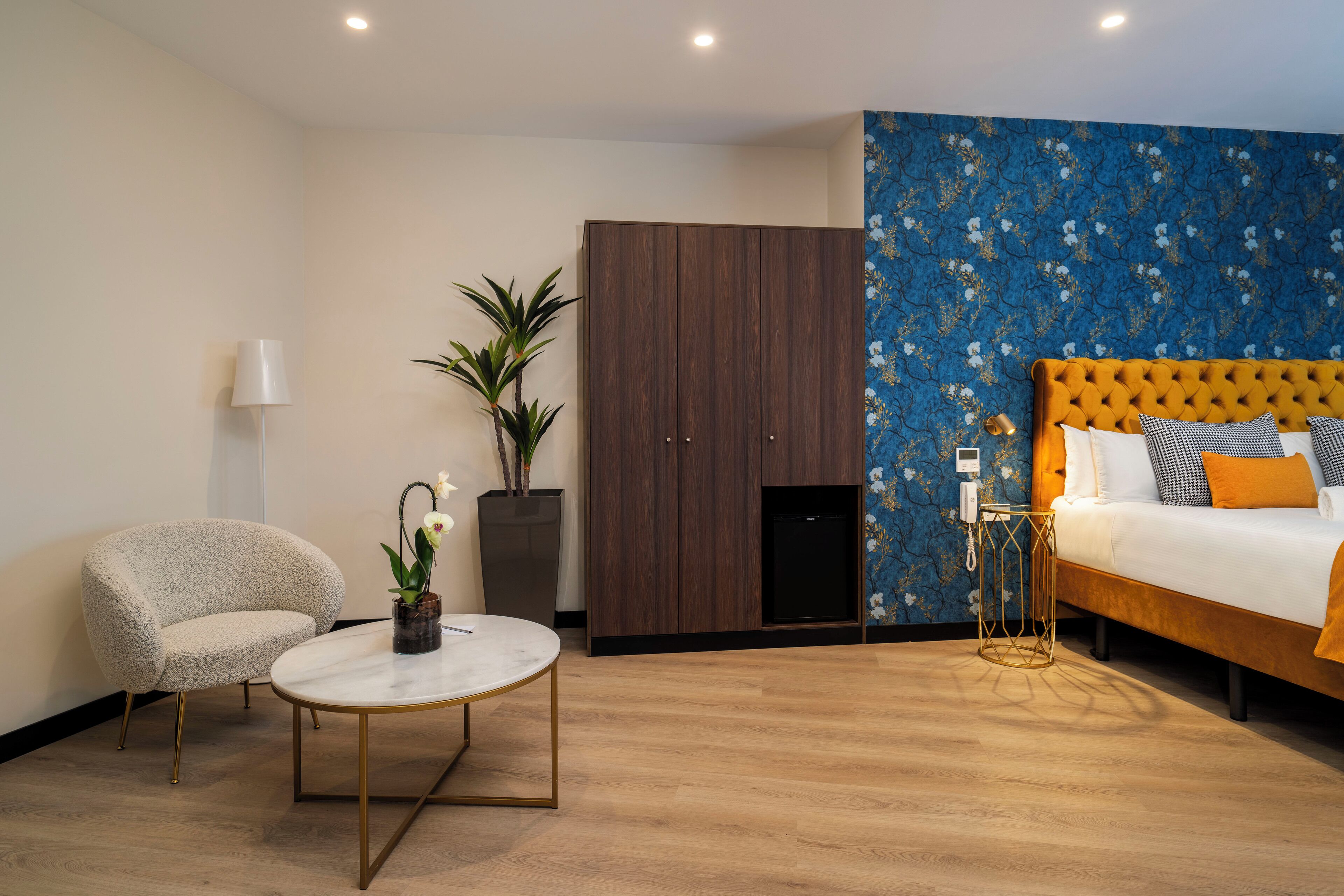 A modern hotel room with a bed, a round table, a chair, a wardrobe, and a potted plant.