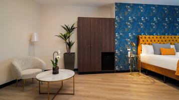 A modern hotel room with a bed, a round table, a chair, a wardrobe, and a potted plant.