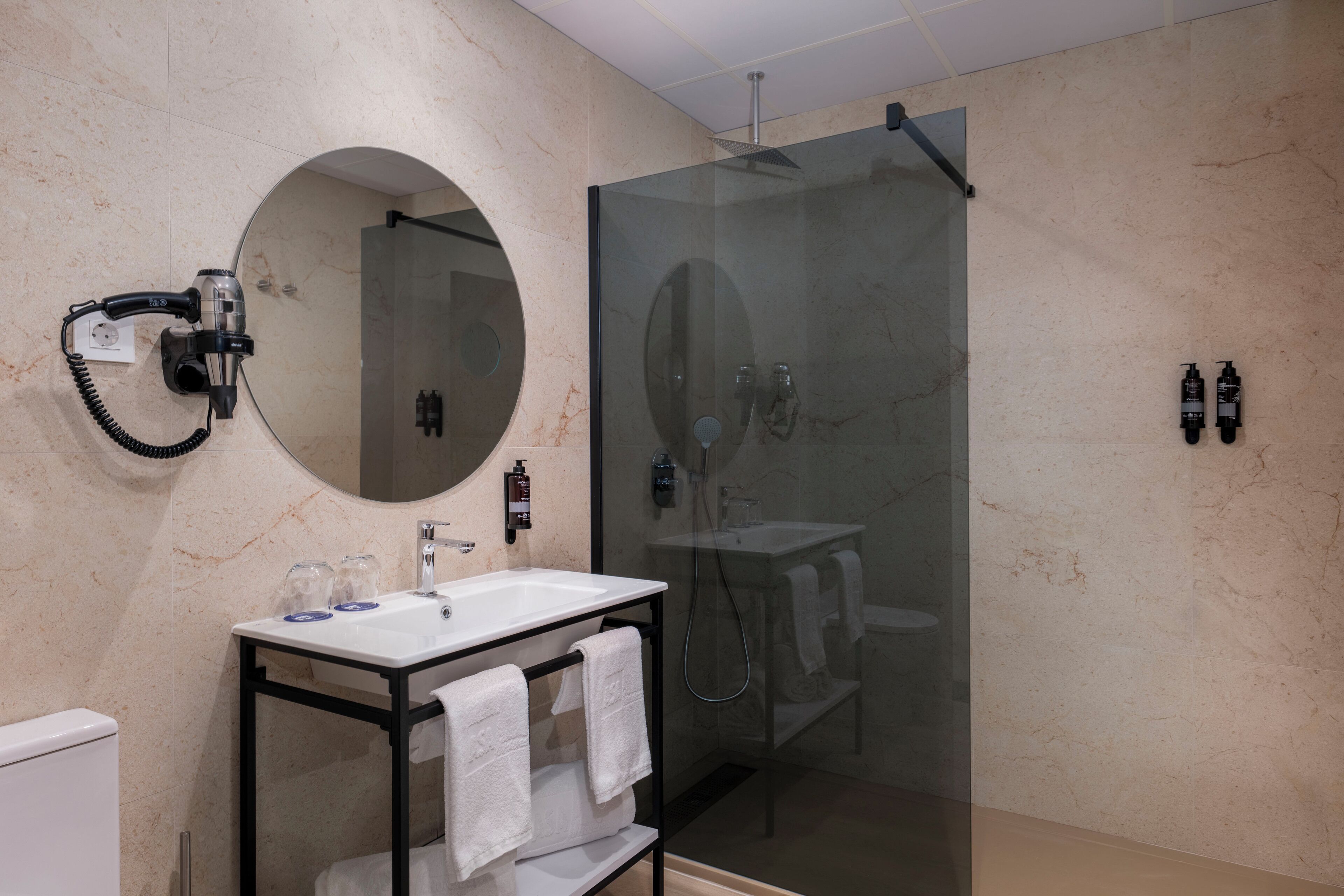 Un baño moderno con ducha de vidrio, espejo redondo y tocador con lavamanos y barra para toallas.